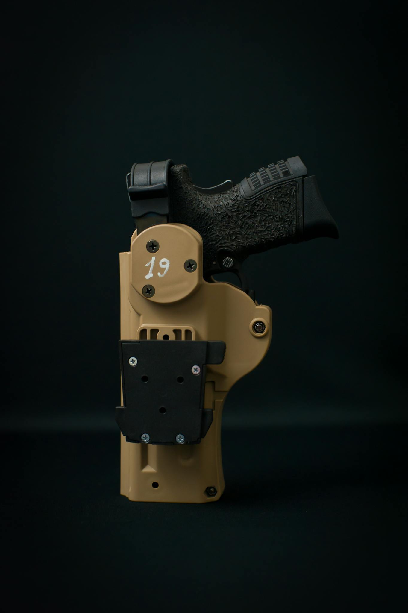 Close-up of a black handgun secured in a tan tactical holster against a black background.