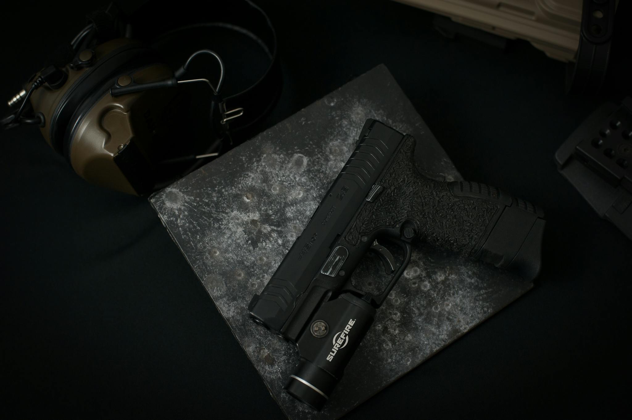 Detailed view of a black handgun with attached tactical flashlight on dark textured surface.